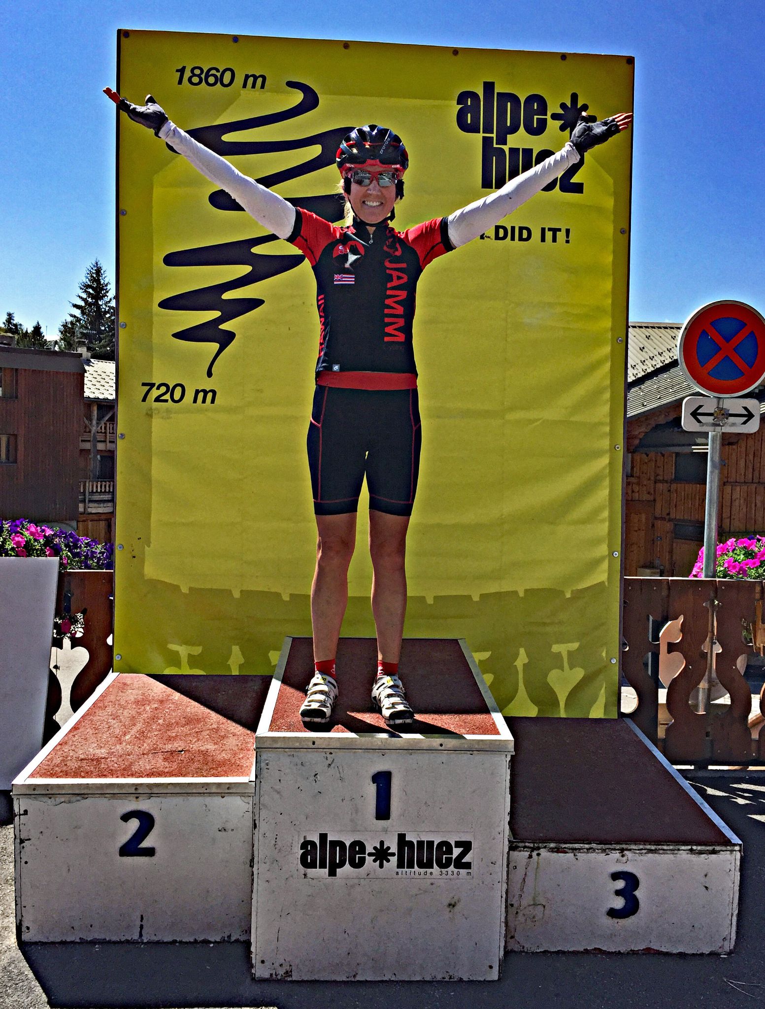 PJAMM Cyclist stands on top of winner's box at Alpe Huez finish line