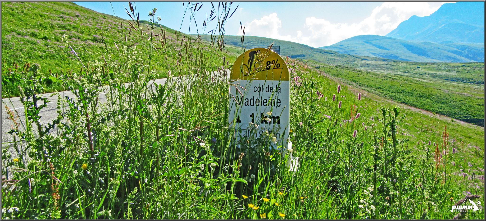 wild grasses partially cover col de la Madeleine 1 km marker on roadside