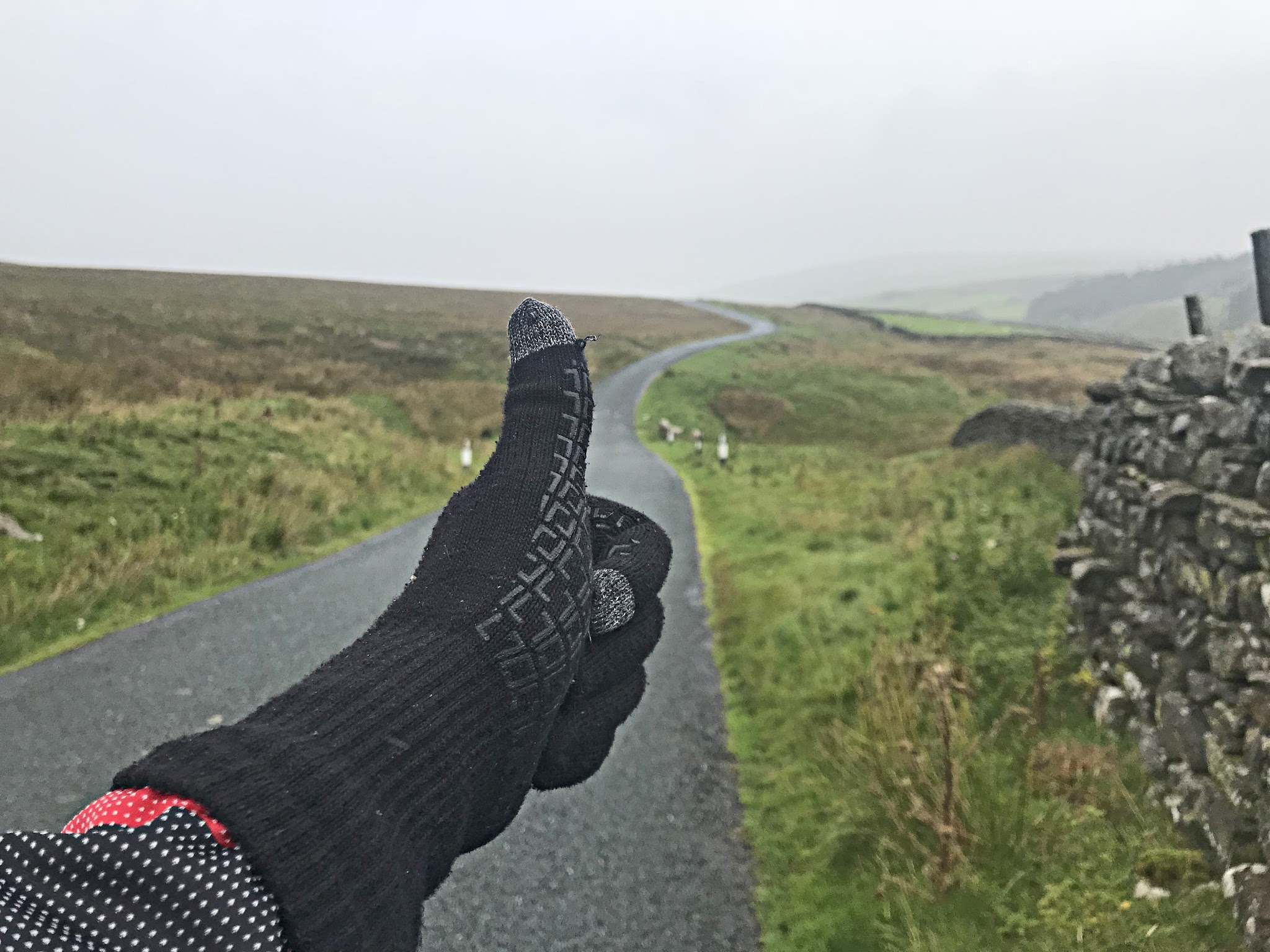 Cycling Tan Hill, UK - gloved hand giving thumbs up to stretch of long narrow roadway through pastureland