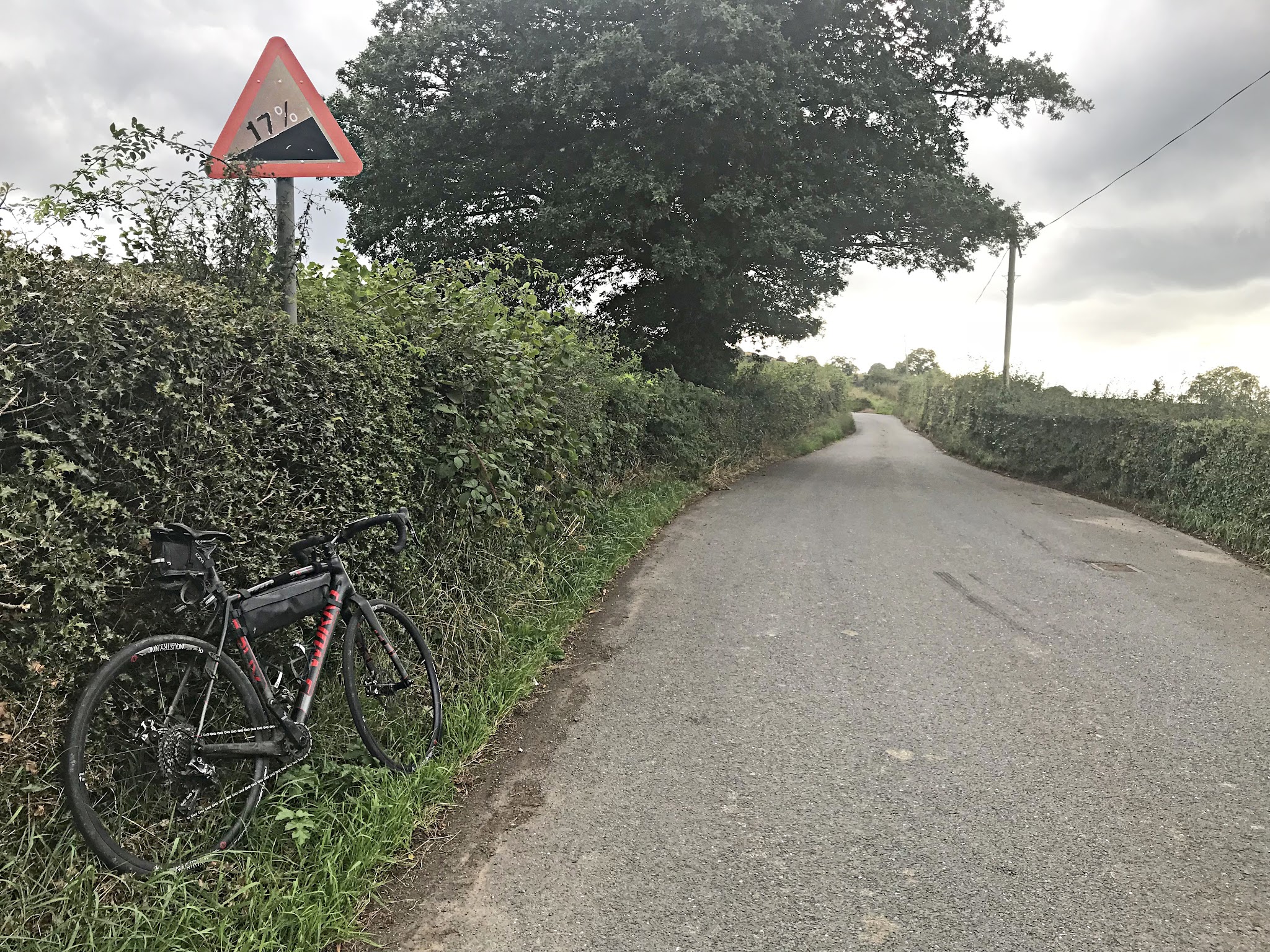 Cycling The Road to Hell, Wales - bike parked in hedges next to 17% grade road sign along edge of one-lane roadway