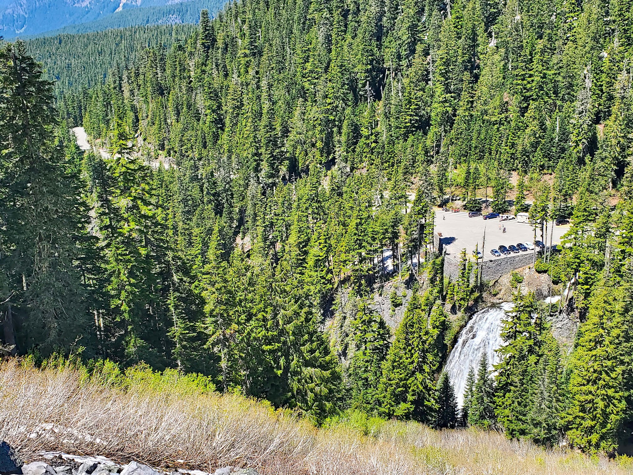 Cycling Mt. Rainier from Nisqually River Entrance looking down on Narada Falls and the Paradise Road from above, parking lot and falls can be seen among thick evergreen tree forestation

