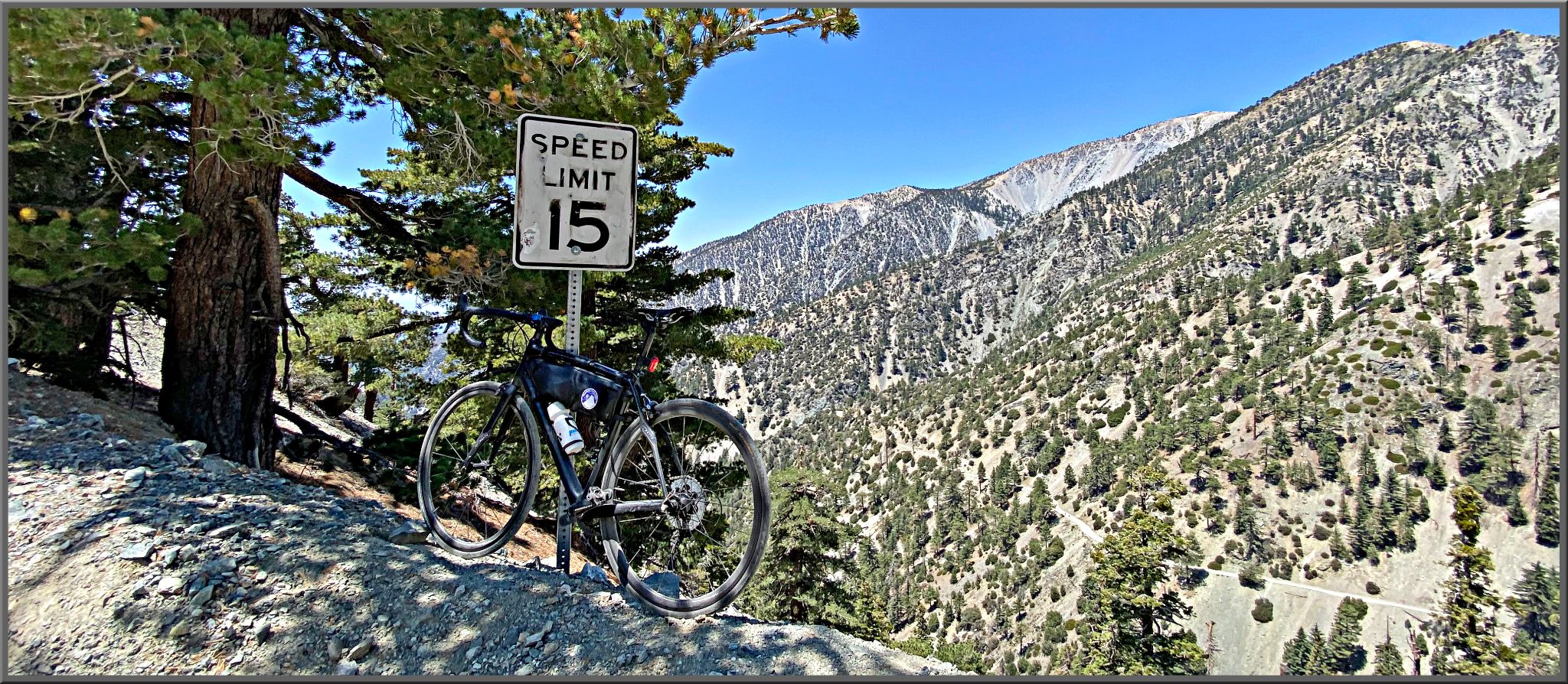 Bike parked on embankment on roadside next to speed limit sign for 15 MPH, Sierra Nevada mountains beyond, evergreen trees, Mt. Baldy rode bike climb