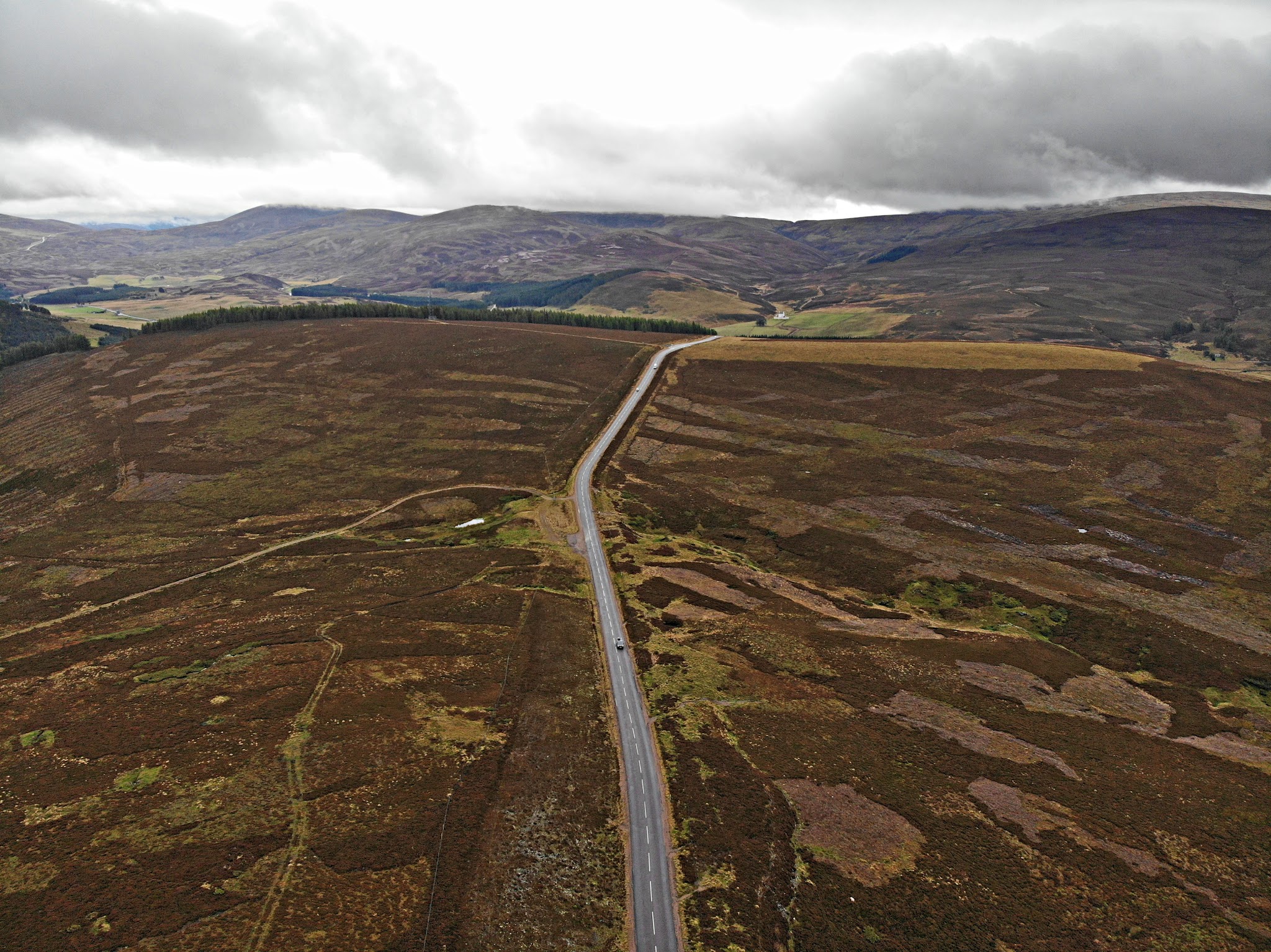 Cycling Lecht Road, Scotland - aerial view of road down center of hillside, grey skies, rolling brownish green hills and pastureland
