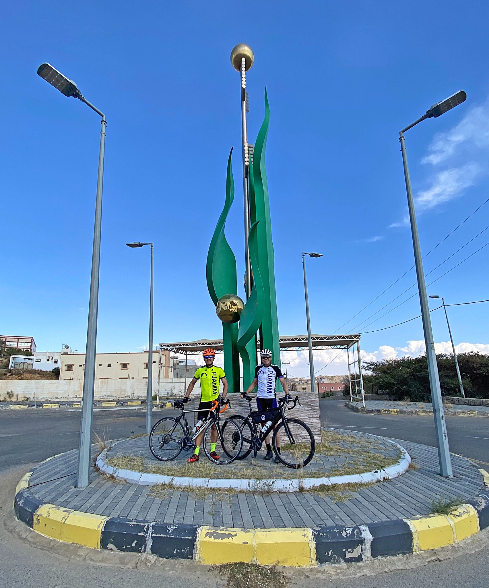 Cycling Bashout Pass, Saudi Arabia - two PJAMM Cyclists stand with bikes in center of roundabout at climb finish