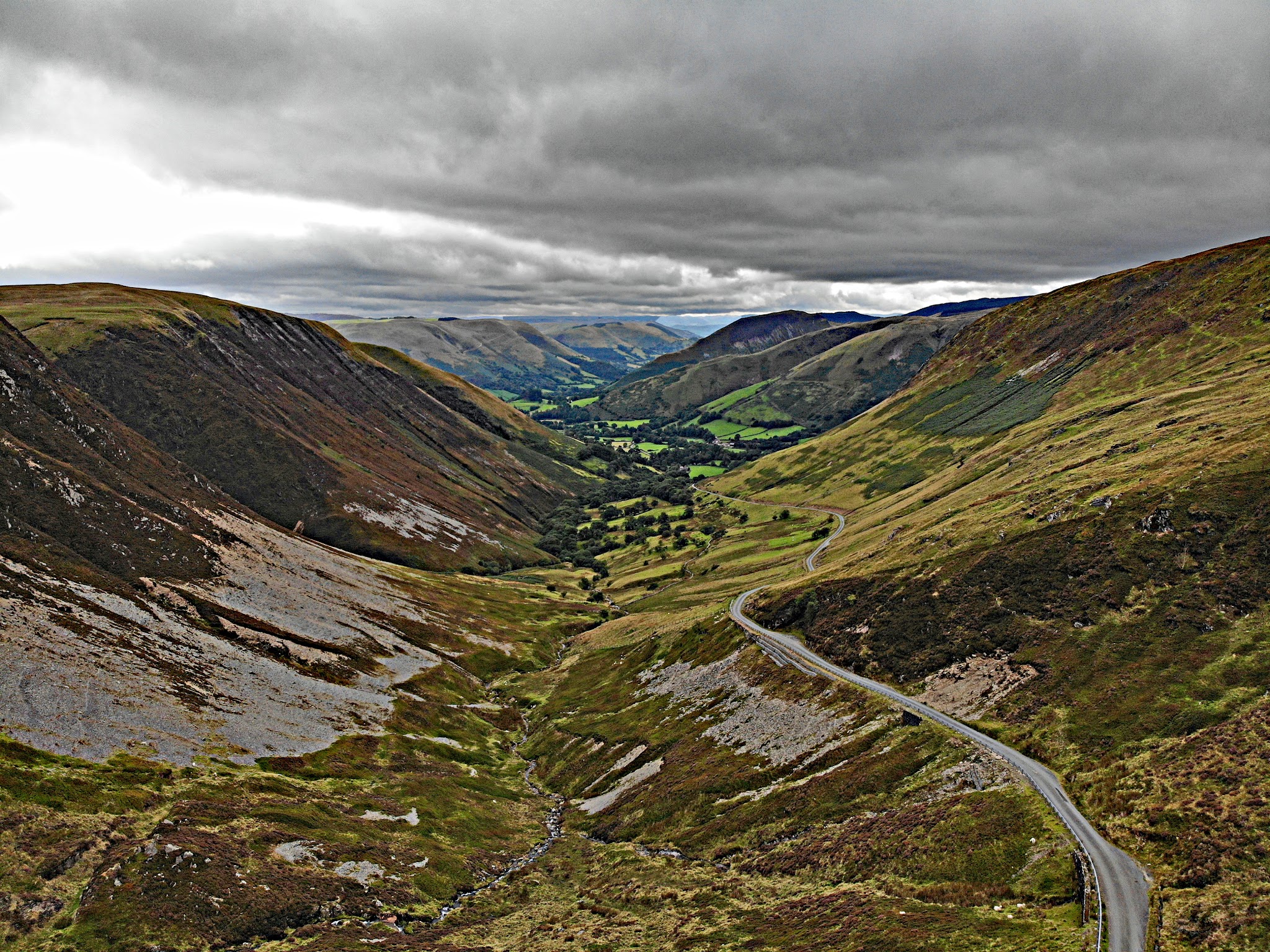 Cycling Bwlch y Groes - View from hilltop overlooking dale with road carved out of hillsides, green and brown pastureland