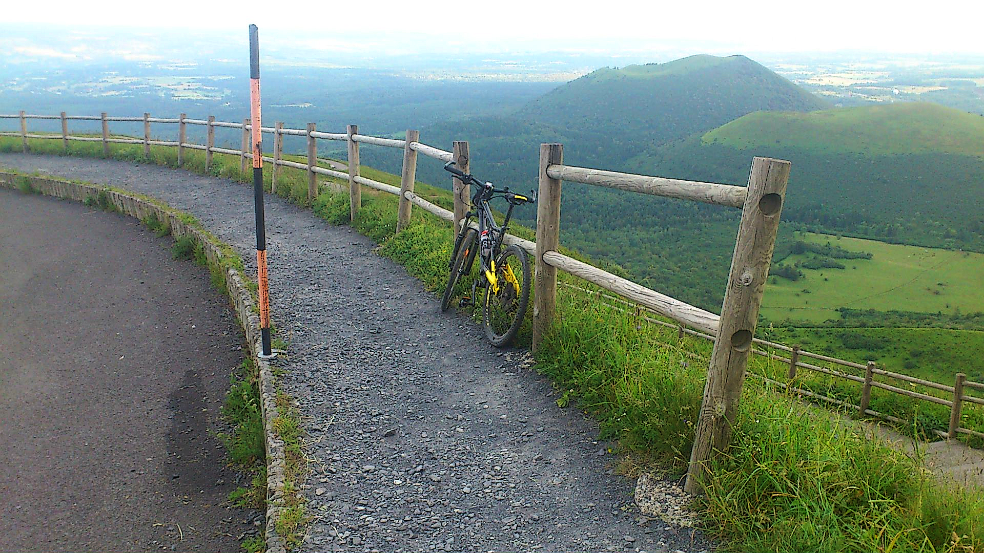 bike parked against wooden fence at climb's finish, looking out over multiple other green-capped volcanoes