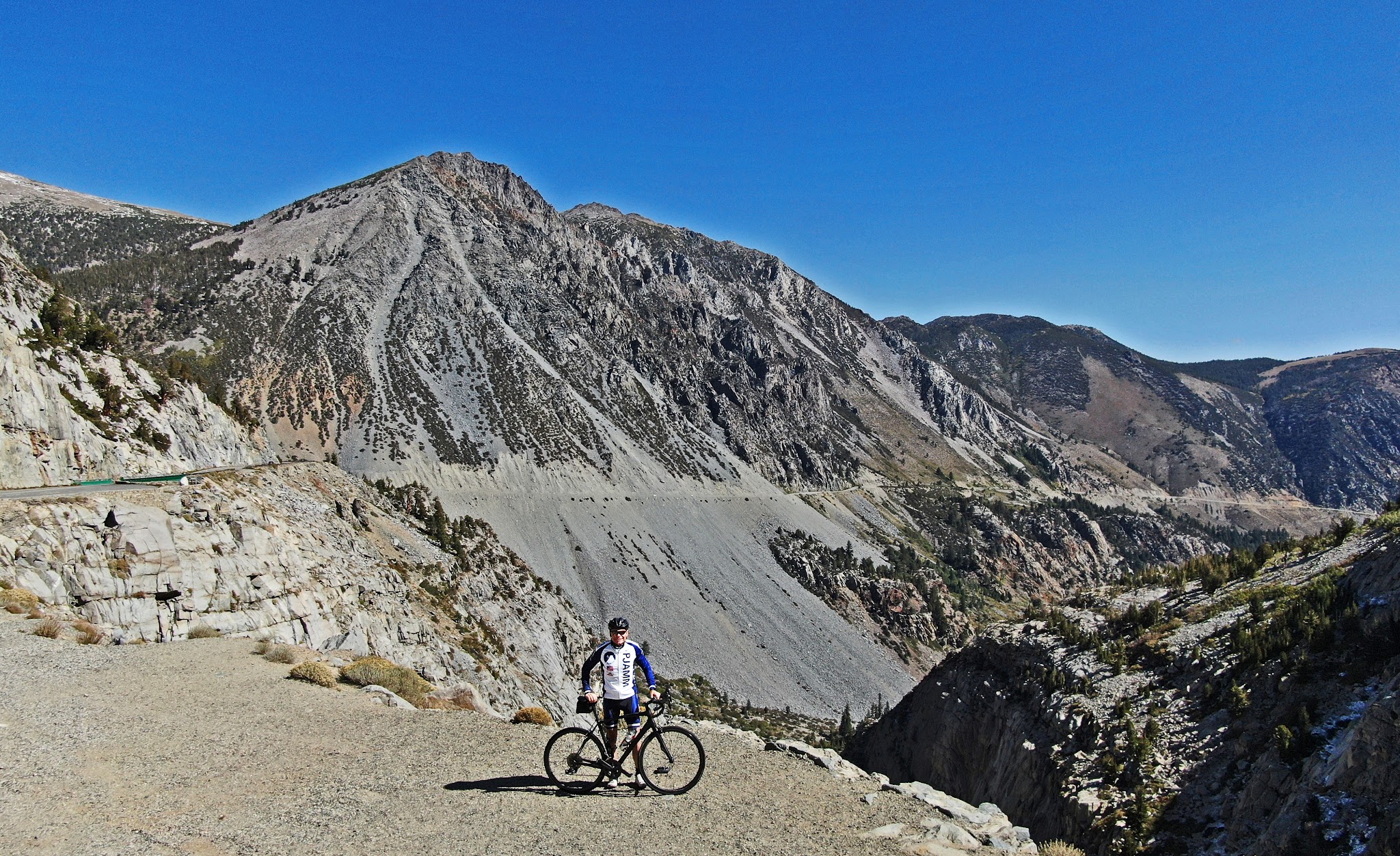 PJAMM Cyclist stands with bike on mountainside, Tioga Pass, amazing rock formations