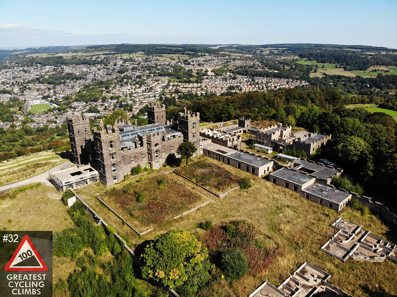 Cycling Riber, England - aerial drone view of Riber castle and the surrounding grounds, town in background, Simon Warren's 100 Greatest Cycling Climbs #32 logo in corner