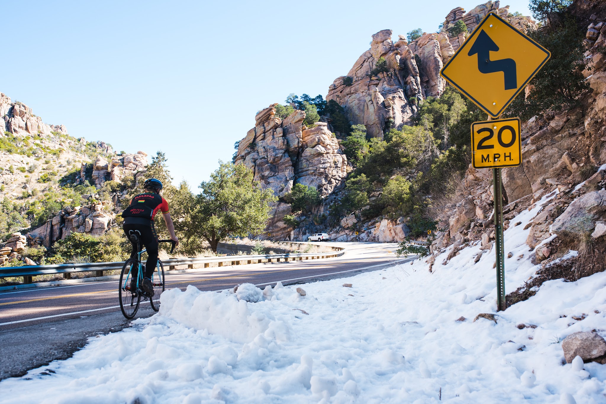 Cyclist riding bike on Mt Lemmon Highway past snow and road sign