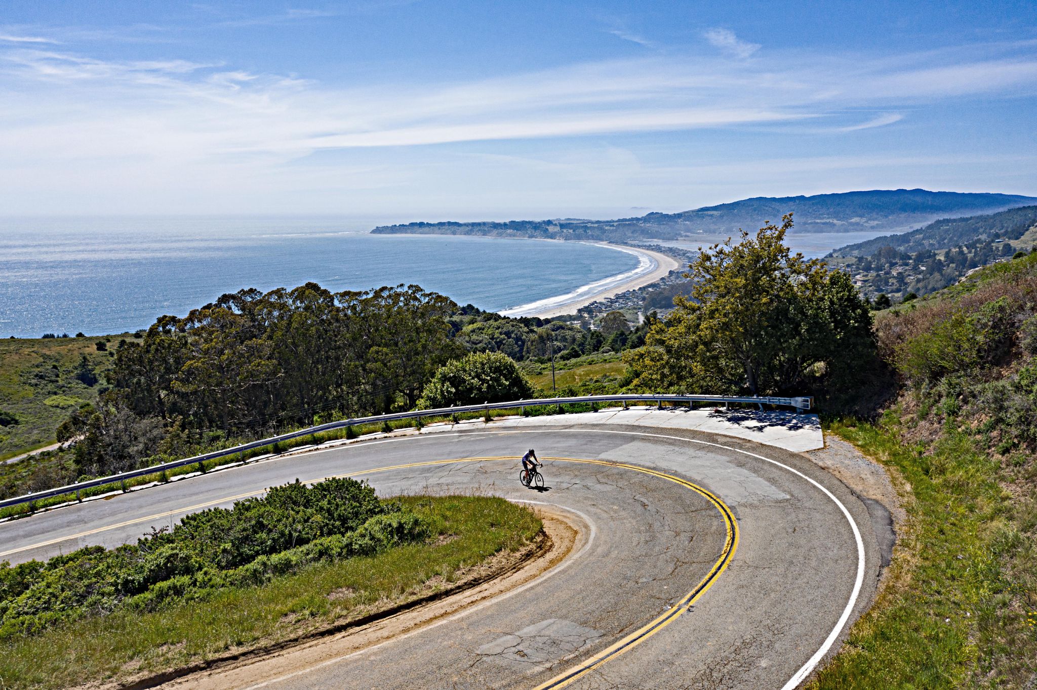 Aerial view of cyclist climb on switchback along roadway, Pacific Ocean in background