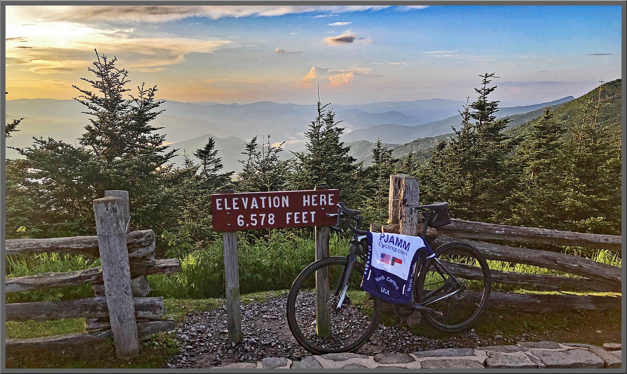 Climbing Mt. Mitchell by bike - bicycle with PJAMM cycling jersey draped over it, elevation sign 6,578 feet, sunrise on mountainside with pine trees