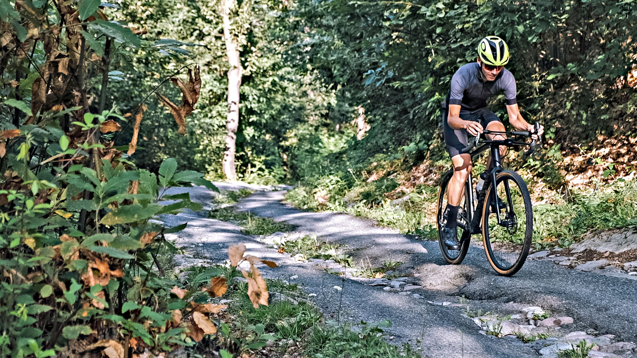 Cycling Pozza San Glisente, Italy - cyclist riding on one-lane, narrow and broken steep rural roadway surrounded by trees