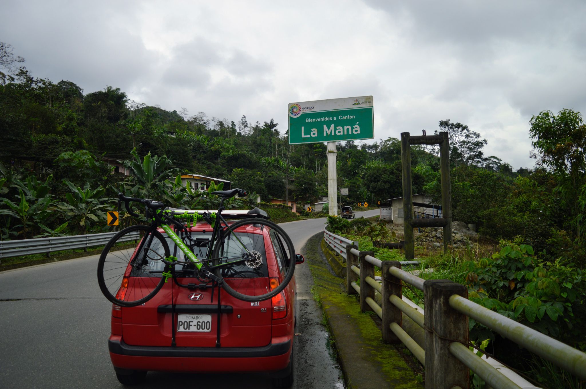 Cycling Apagua, Ecuador  - red SAG vehicle with bikes strapped to back parked on road side next to green sign for La Mana