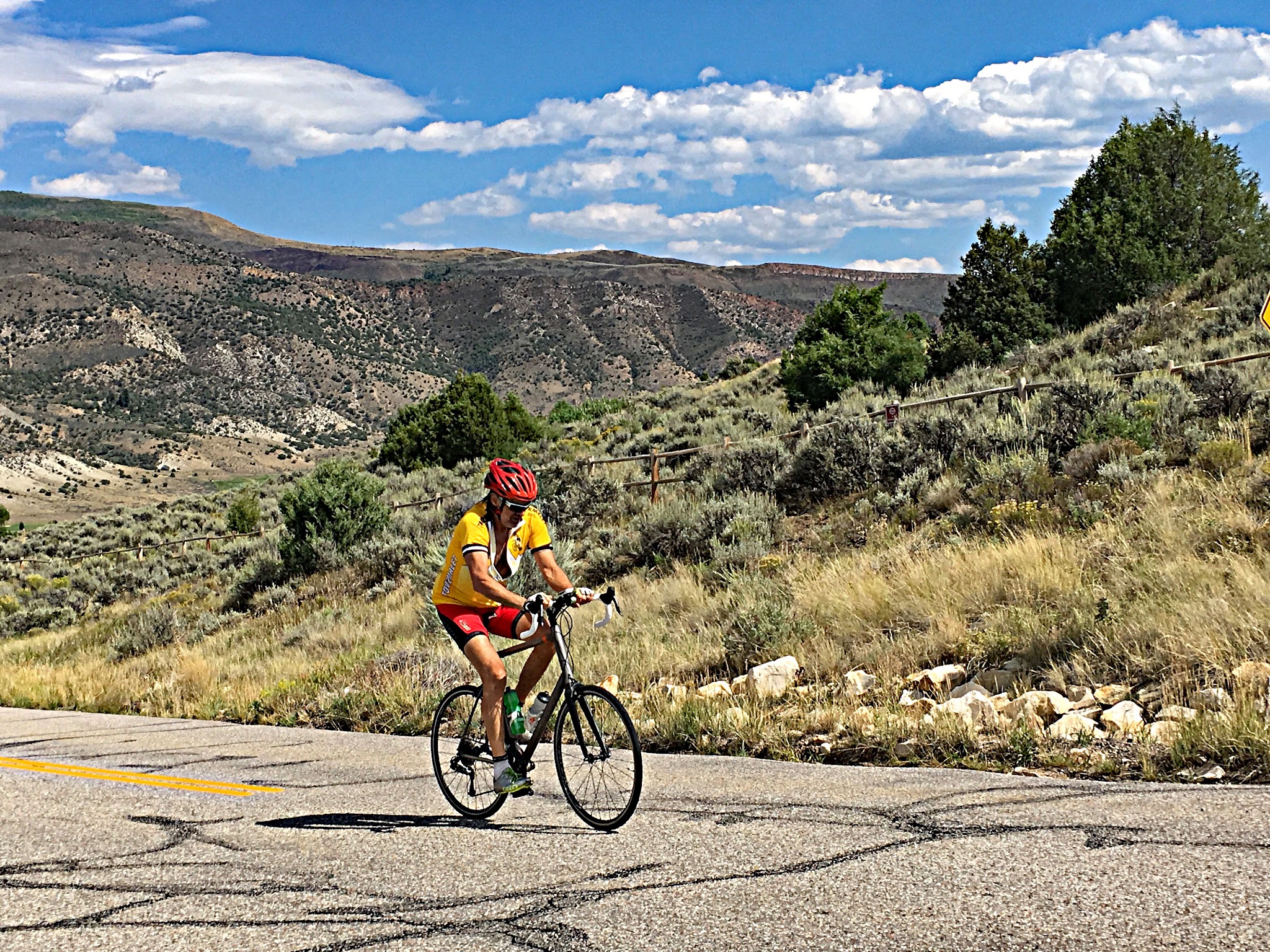 Cycling Bellyache Ridge, Colorado - cyclist Mike Persellin climbing on roadway surrounded by scrub brush and low mountains, blue sky beyond