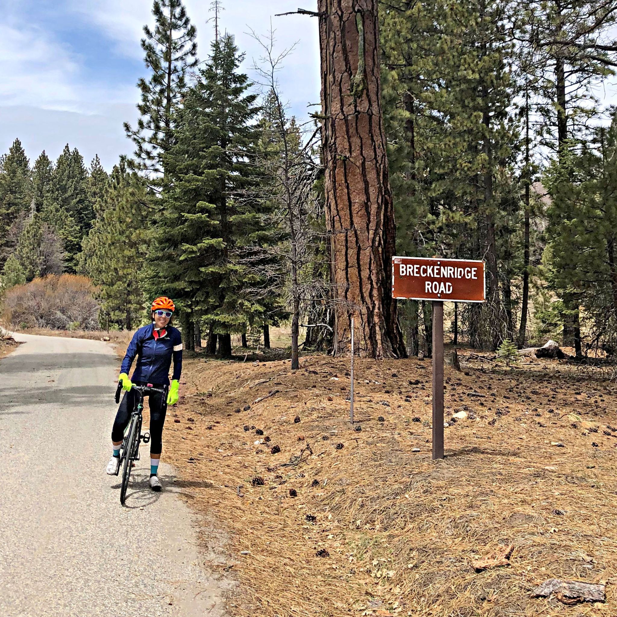 Cycling Breckenridge West, California Cycling Breckenridge West, California - Cyclist Lisa Irizarry stands on bike next to sign for Breckenridge Road, alpine setting, pine trees