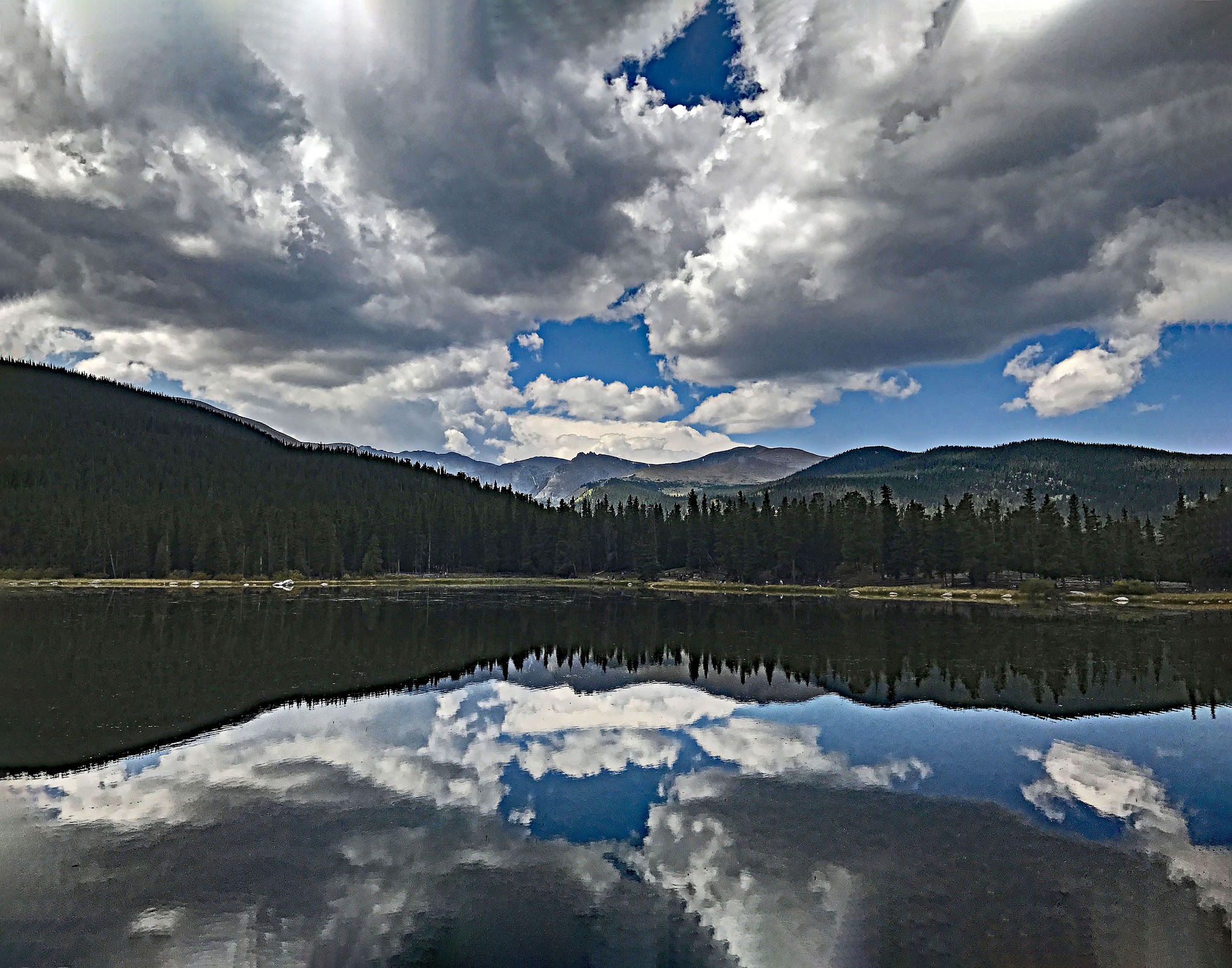 Cycling Juniper Pass West - crystal clear reflection on Echo Lake showing blue sky with fluffy white clouds, mountain range, and spiky evergreen trees