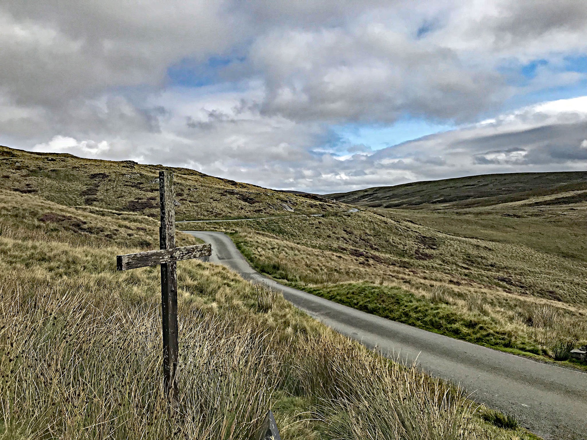 Cycling Bwlch y Groes - narrow one lane road winds through brown pastureland with small, rustic wooden cross staked along roadside