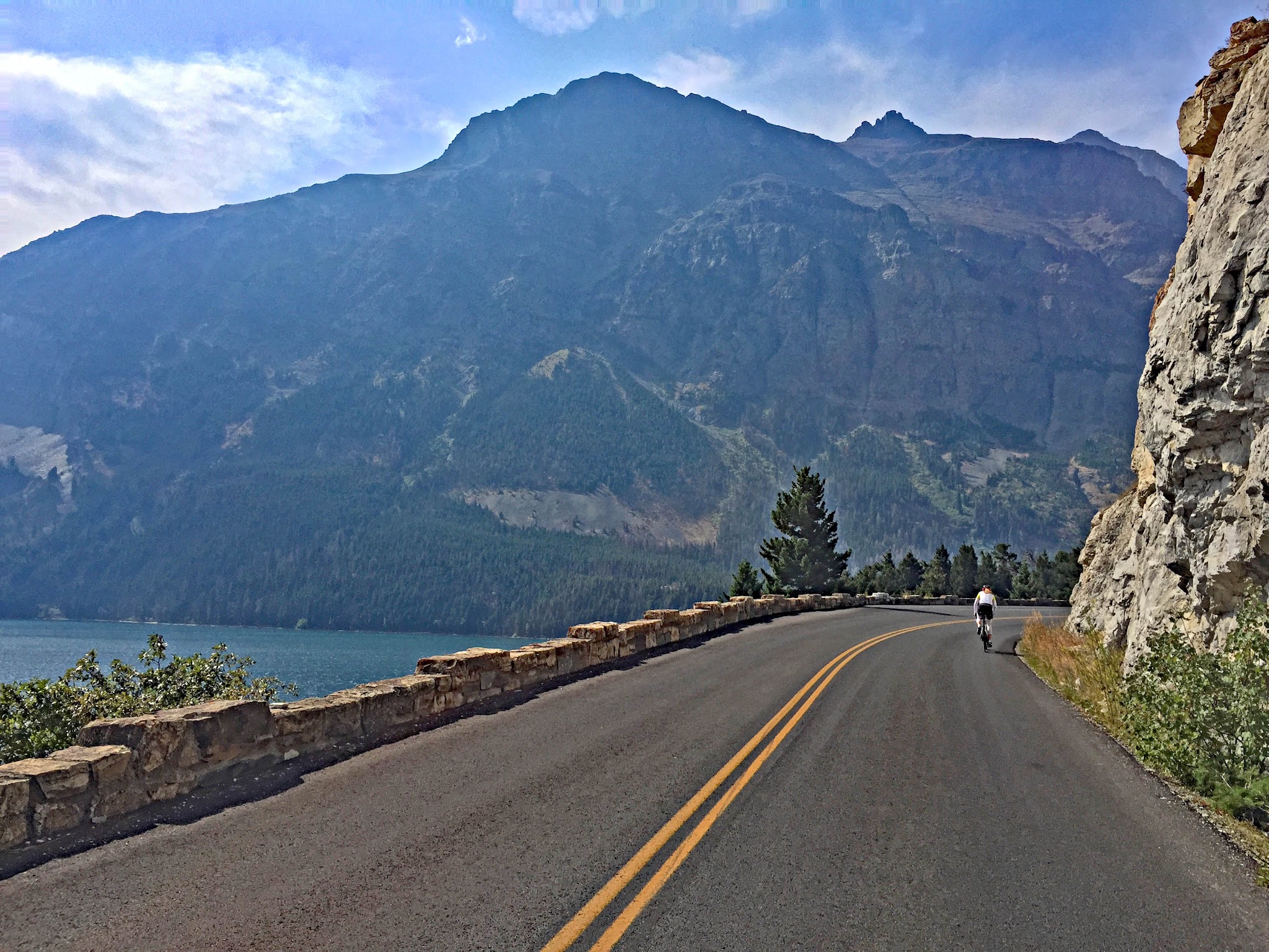 Cycling Logan Pass East, Going-to-the-Sun Road, Glacier National Park - cyclist riding on two-lane portion of road along Saint Mary Lake, riding toward large rock formations