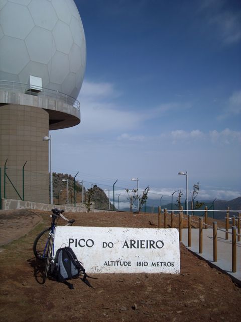 bike and backpacked parked in front of white stone sign for Pico do Arieiro