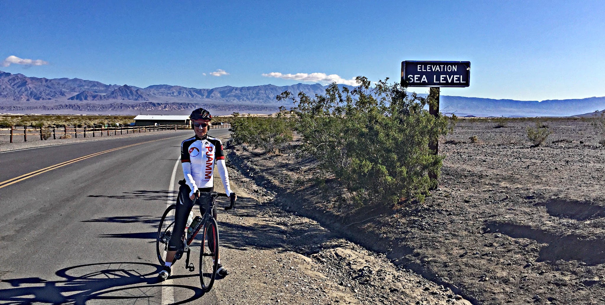 California's most epic bike climbs - Emigrant Pass, Death Valley National Park - climb by bike - cyclist in Stovepipe wells at Sea Level sign