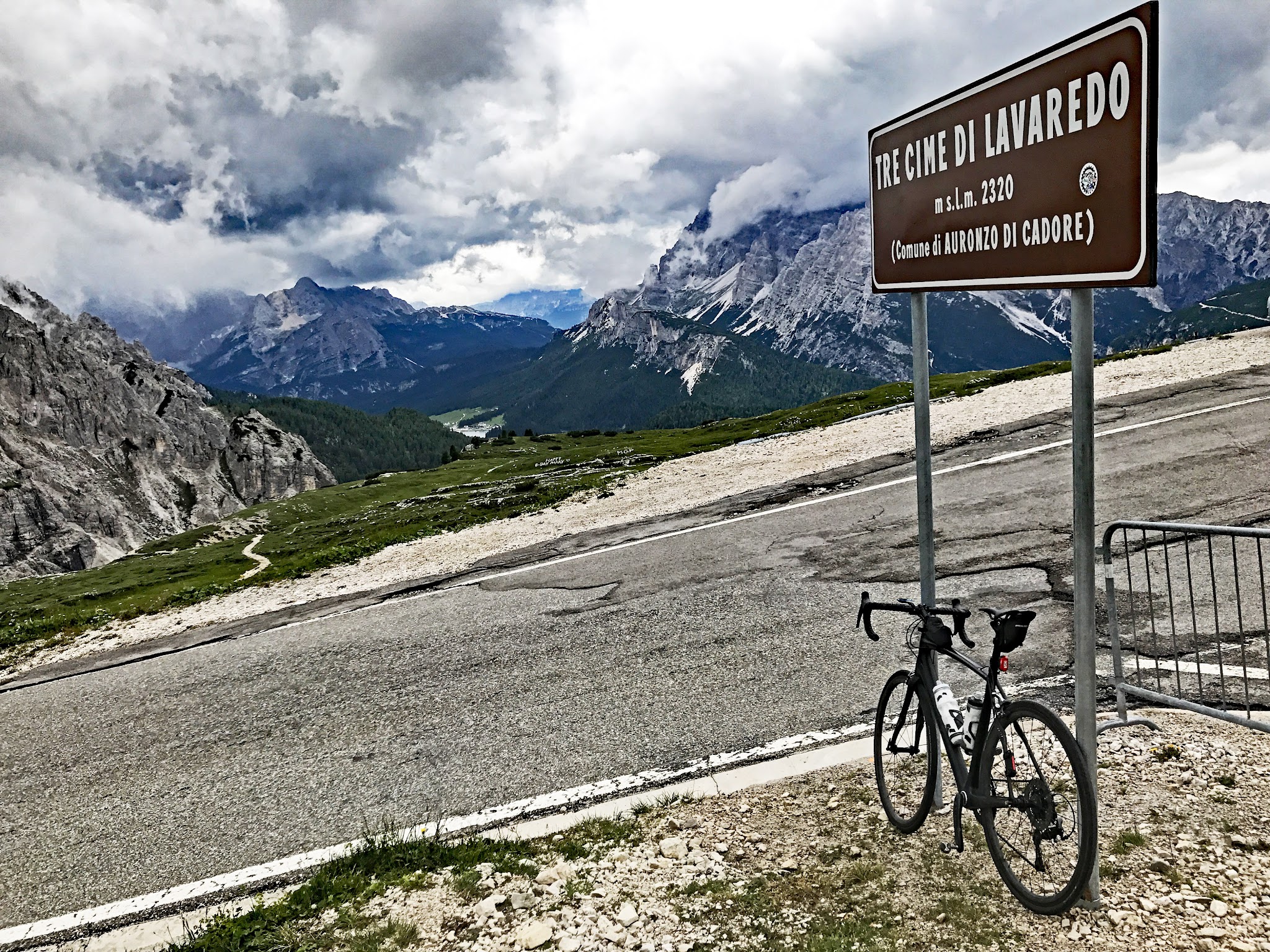 Cycling Tre cime di lavaredo - summit sign with bike leaning on sign, mountains in background