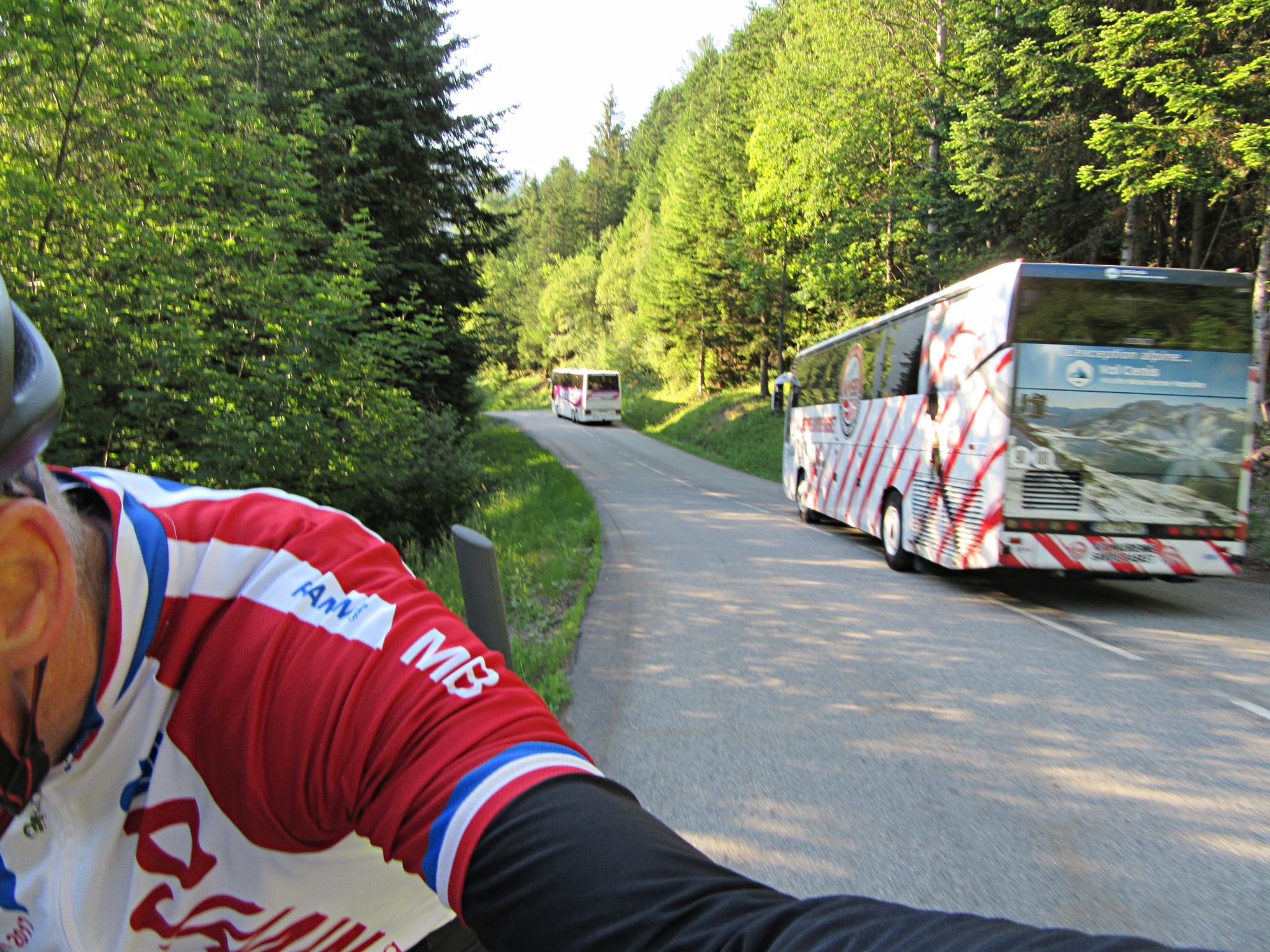 Cycling Col du Galibier & Telegraphe: PJAMM Cyclist rides on side of roadway and takes selfie showing two tour busses passing him