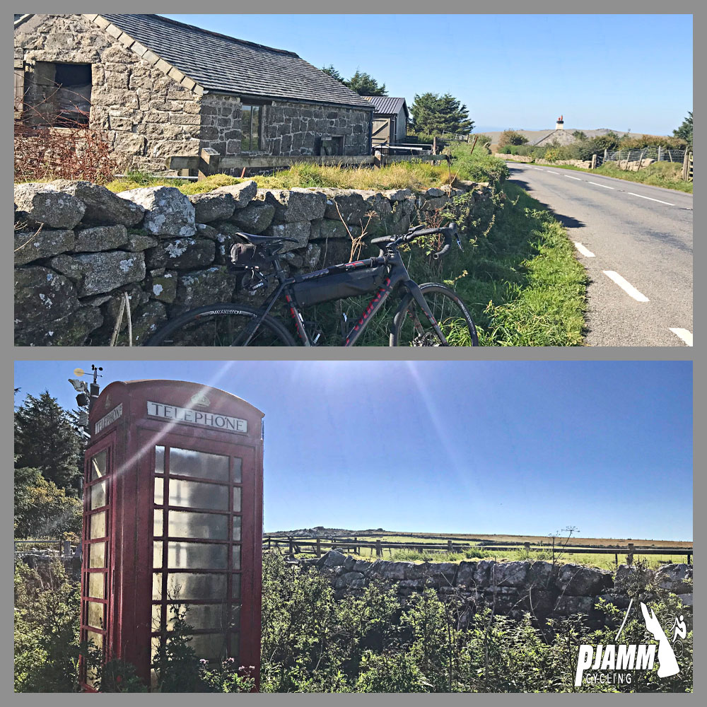 Cycling Rundlestone, England - low stone wall with road bike parked against it next to two-lane roadway with old stone building on far side of wall, iconic British red telephone booth along roadway next to pastureland, sunny, blue sky above, PJAMM Cycling logo in corner