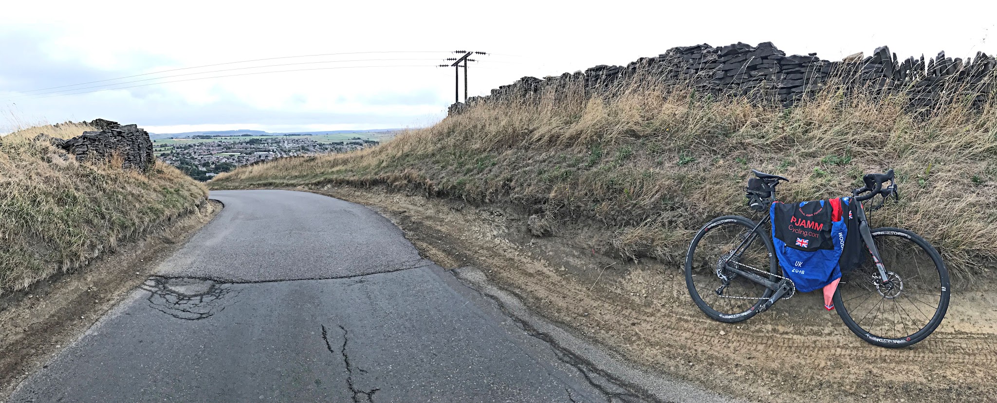 Cycling Pea Royd Lane - bike with PJAMM Cycling jersey draped over it, leaning against tall eroded rock/dirt walls lining narrow one-lane roadway