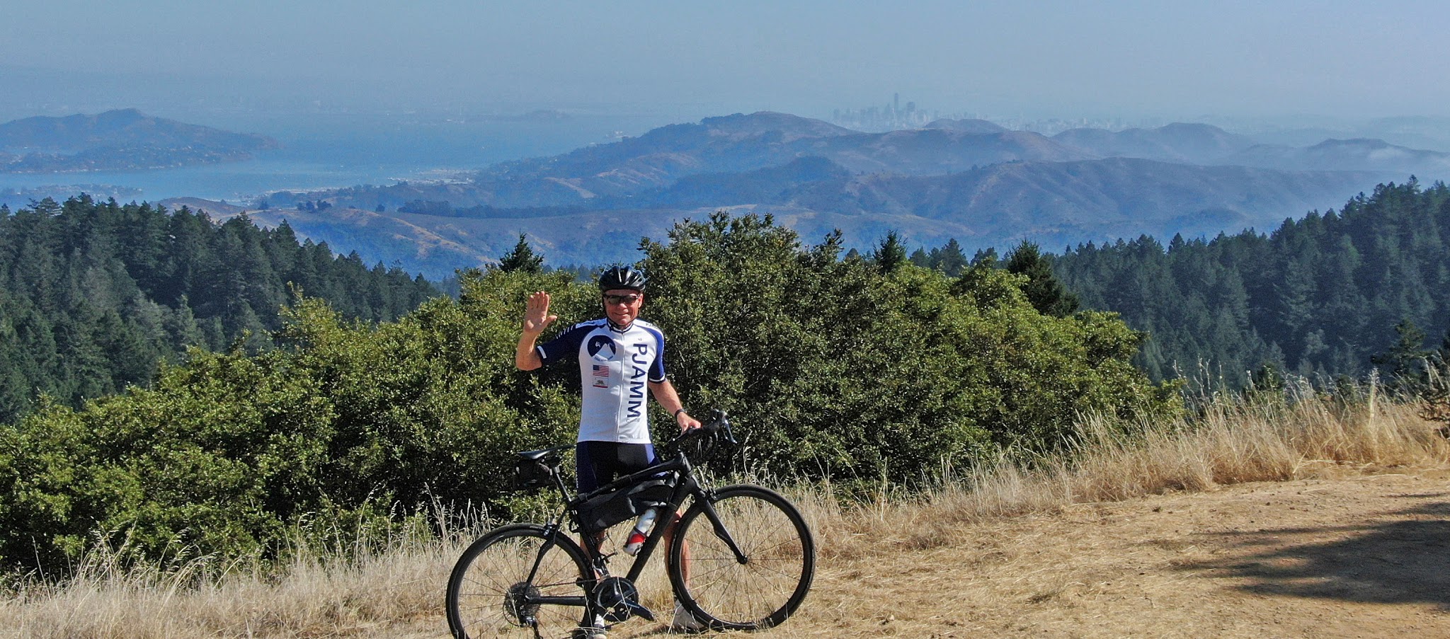 Cycling Golden Gate Bridge to Mt. Tam, California Cycling Golden Gate Bridge to Mt. Tam, California - PJAMM Cyclist John Johnson stands with bike on roadside next to Pantoll Road, San Francisco can be seen in distance