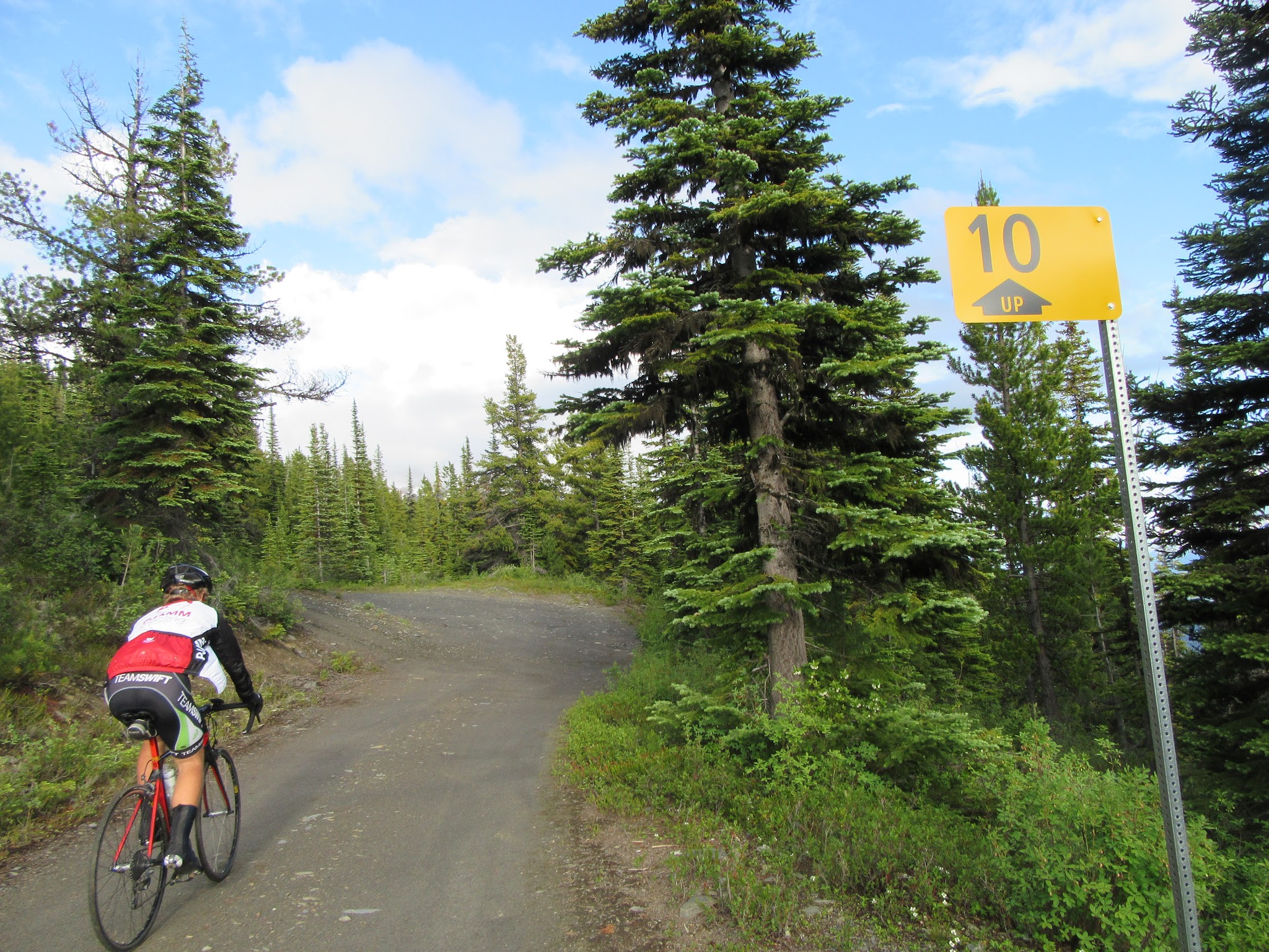 Climbing McBride Peak by bike - cyclist riding past kilometer sign