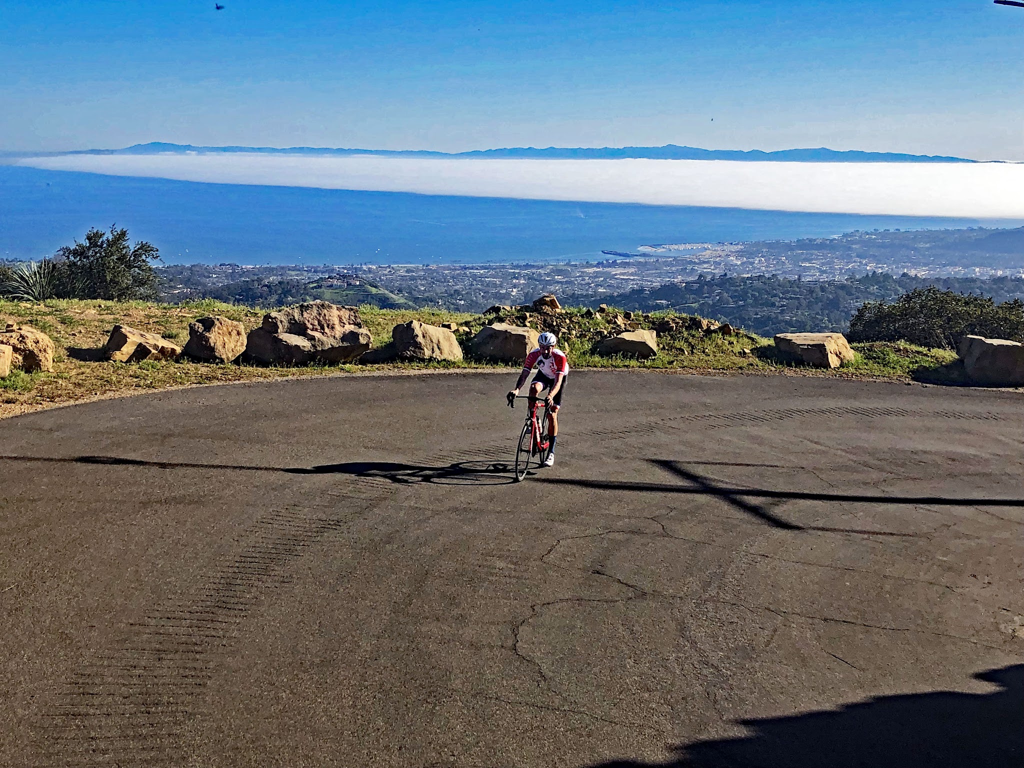 Cycling Southern California - Gibraltar Road, cyclist rides on wide area of road curving uphill,  Santa Barbara in the background