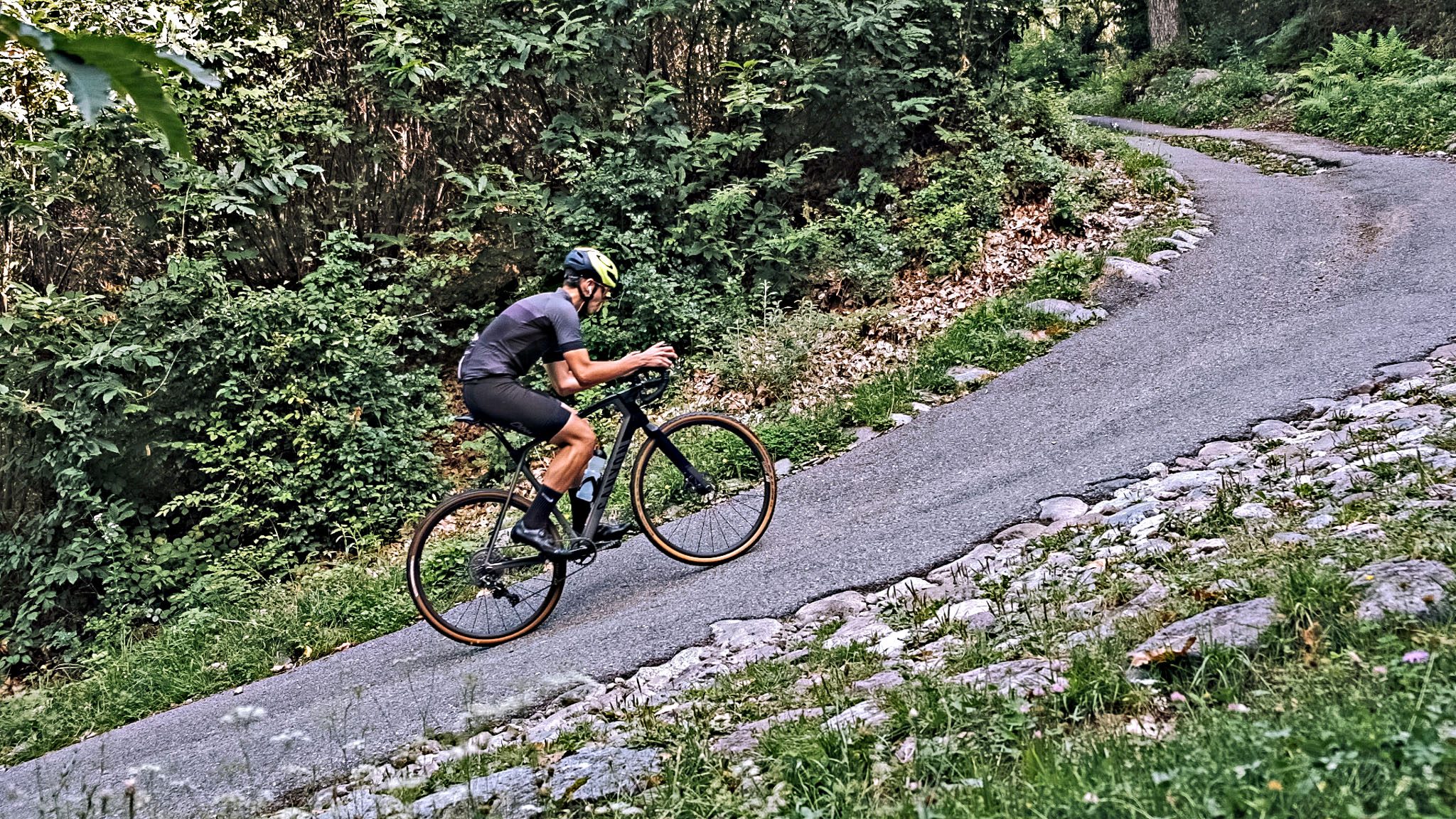 Cycling Pozza San Glisente, Italy - cyclist riding on one-lane, narrow and steep rural roadway surrounded by trees