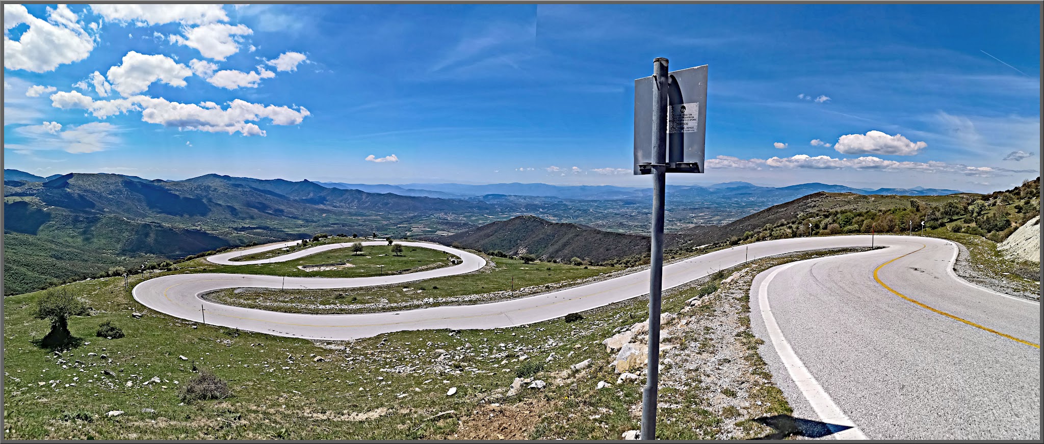 Cycling Mount Olympus, Greece - two-lane roadway snakes it's way up mountainside with green grace, blue sky and mountains beyond