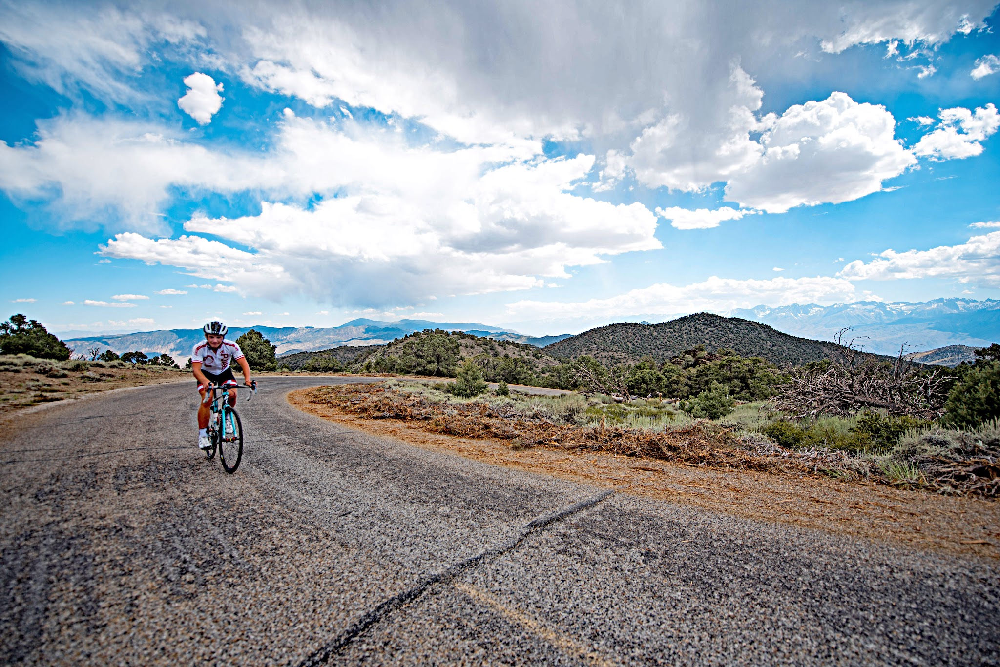 Cycling White Mountain, California - cyclist rides on roadway, high desert landscape, blue sky and white clouds in background