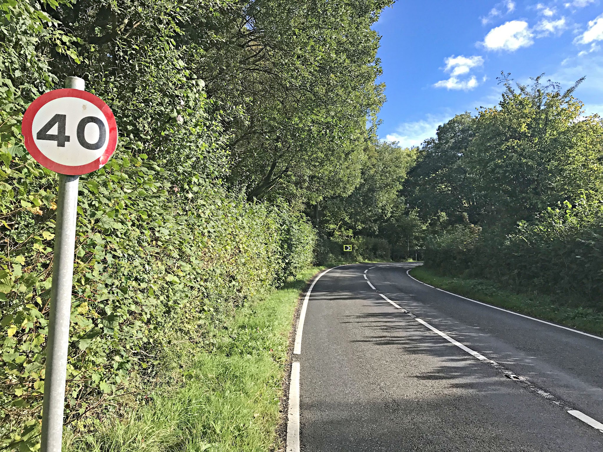 Cycling Black Mountain, Wales - tree/brush-lined two lane road with blue sky in background, road sign for 40 kph