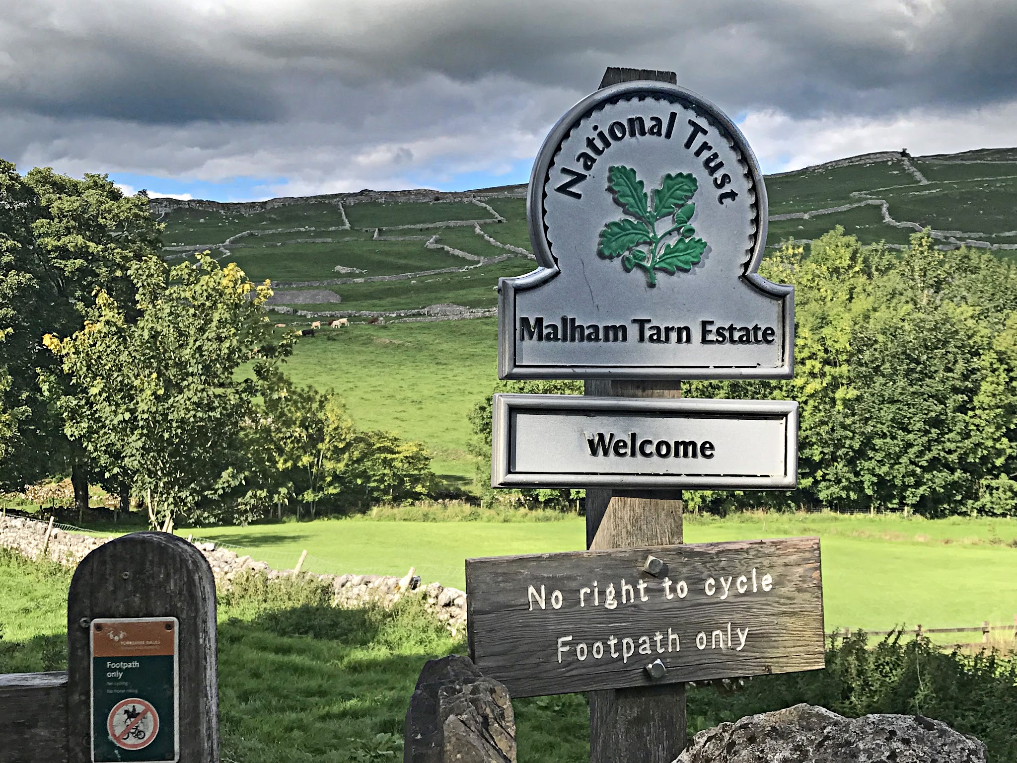 Cycling Malham Cove - National Trust sign for Malham Tarn Estate, in background are sprawling green hills 