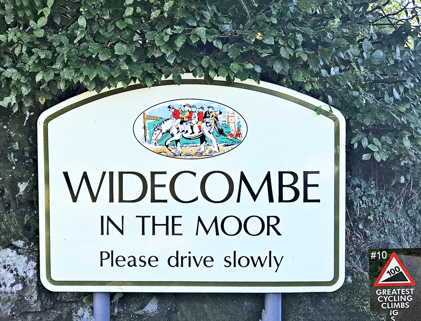 Cycling Widecombe - white road sign saying "Widecombe in the Moor Please Drive Slowly" against green hedge, Simon Warren's 100 Greatest Cycling Climbs Logo #10 in corner