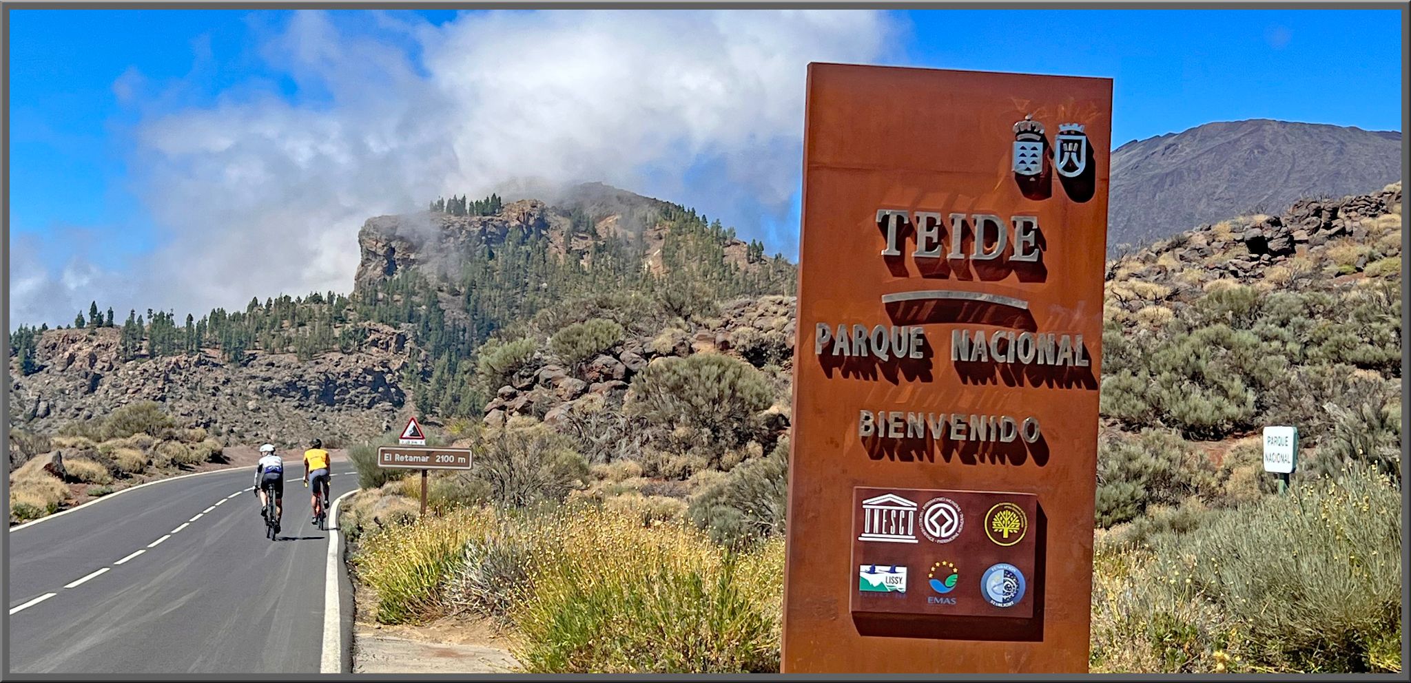 PJAMM Cyclists ride on two-lane highway roadway past Teide Parque Nacional sign