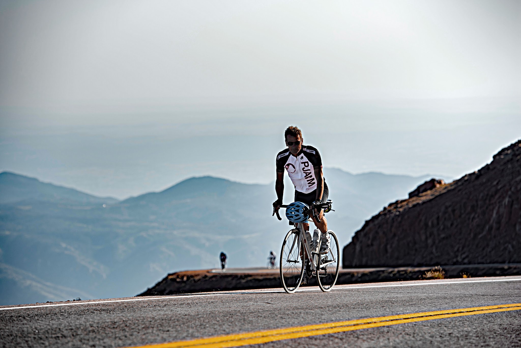 Cycling Pikes Peak - Cyclist climbing stretch of two lane road wearing PJAMM Cycling jersey