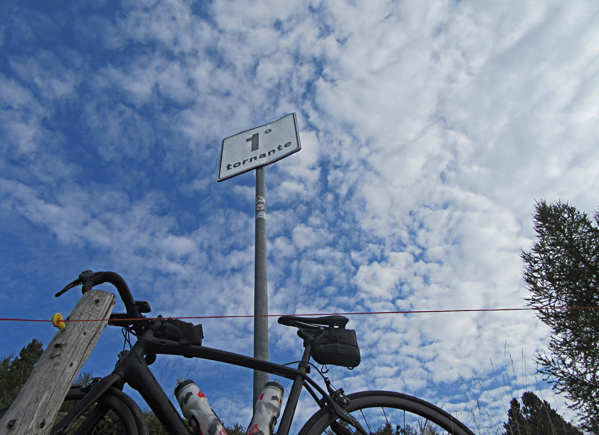 Cycling Passo del Mortirolo from Mazzo di Valtellina - Tornanti (hairpin) #1 sign with bike leaning against sign