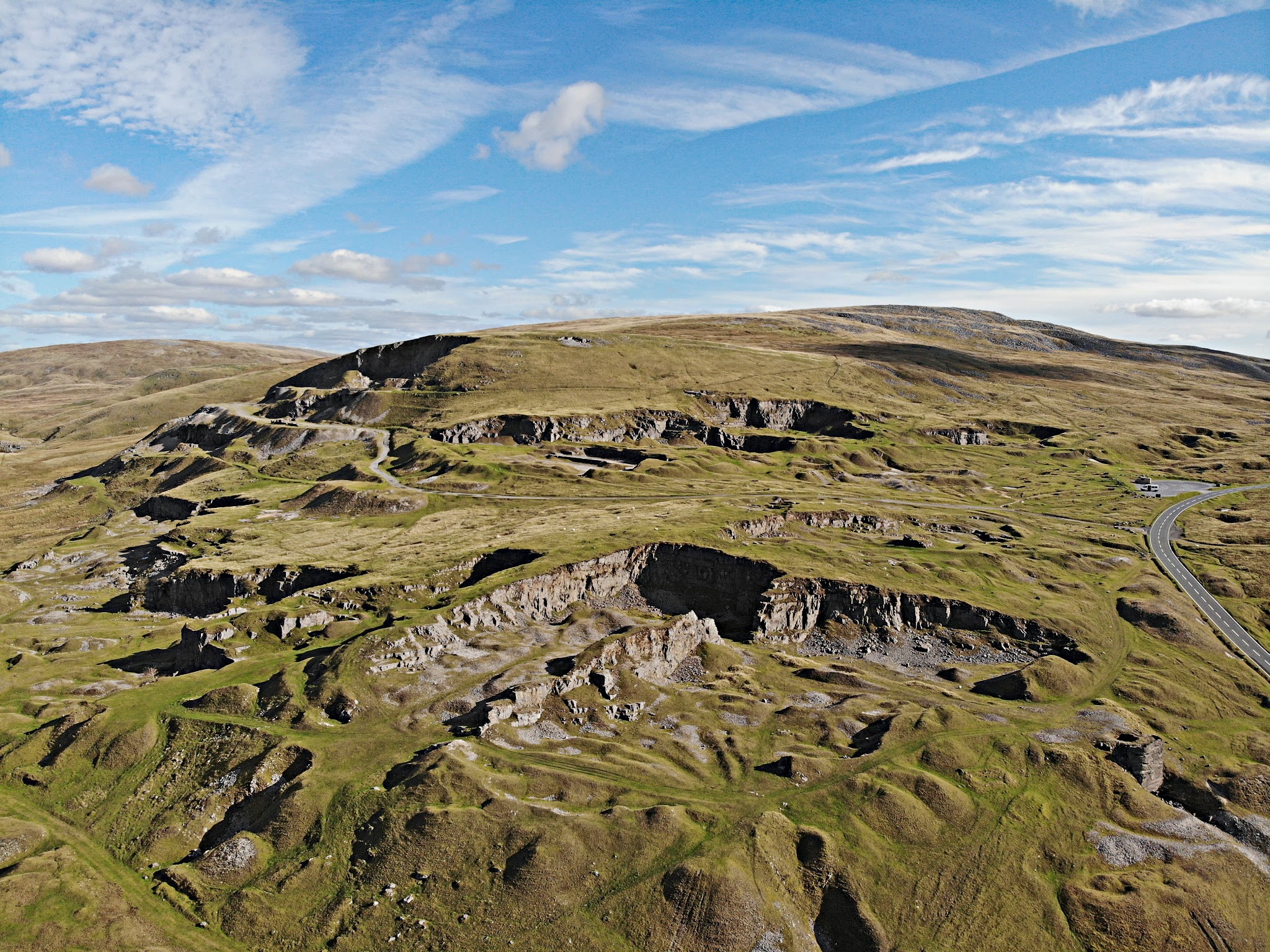 Cycling Black Mountain, Wales - aerial view of Herbert's Quarry along hillside, blue sky, green hillsides, road traveling up right hand side
